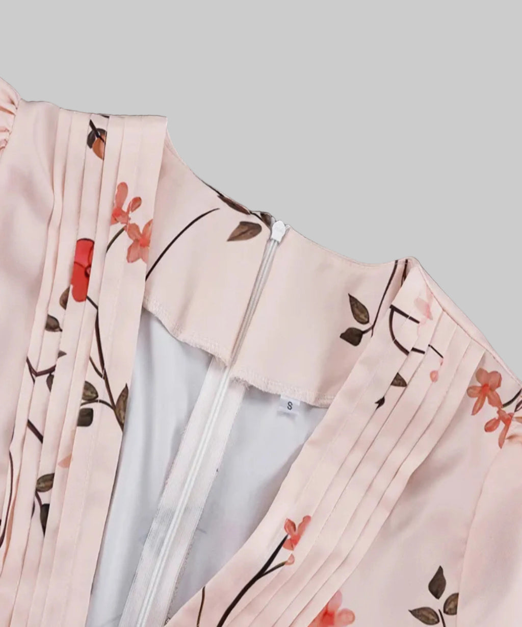 Close-up of a light pink pleated garment with a floral print featuring red flowers and brown leaves, shown against a solid black background.