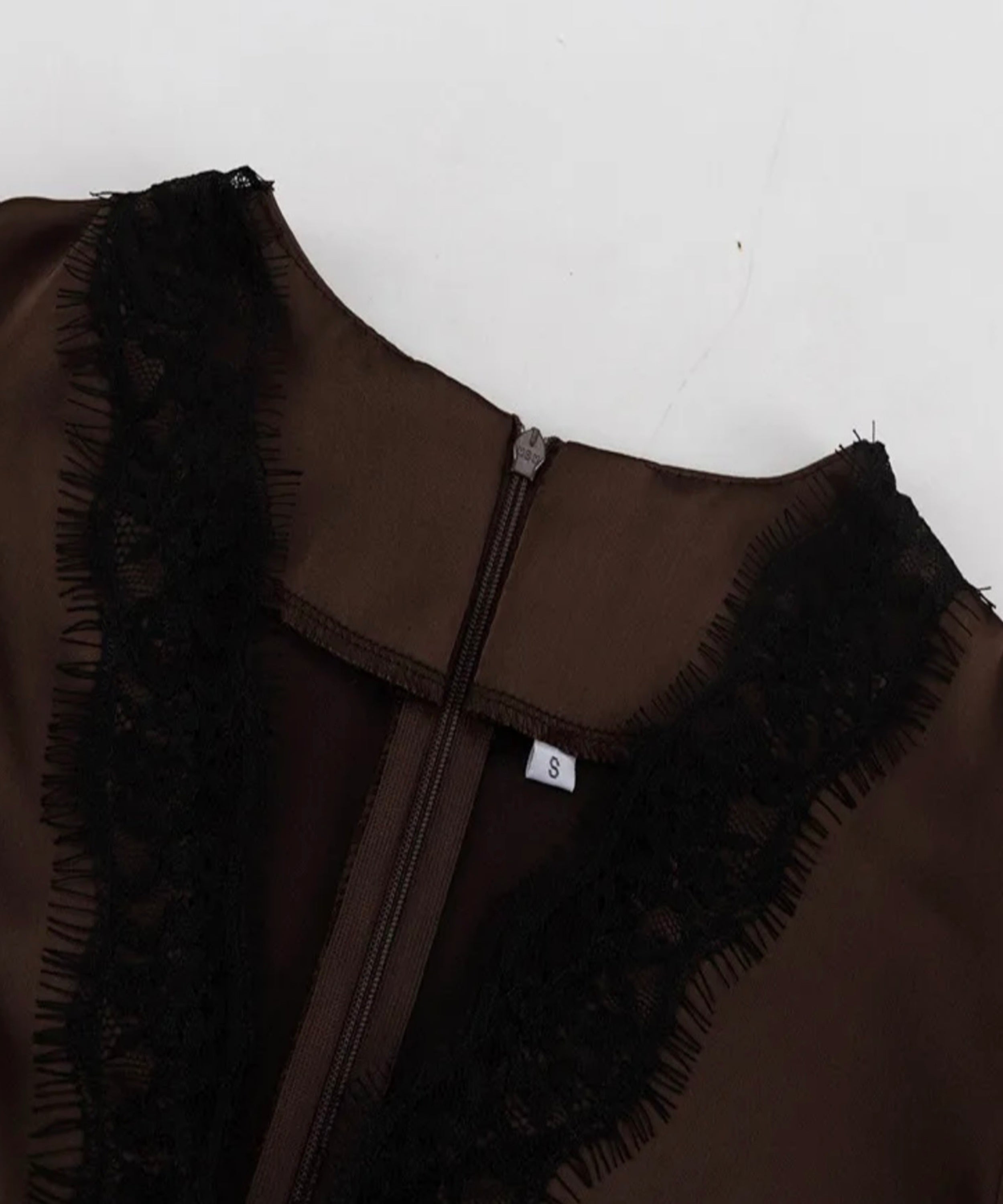 Close-up of a brown satin-like garment with black lace trim and a central zipper, shown against a plain light background.