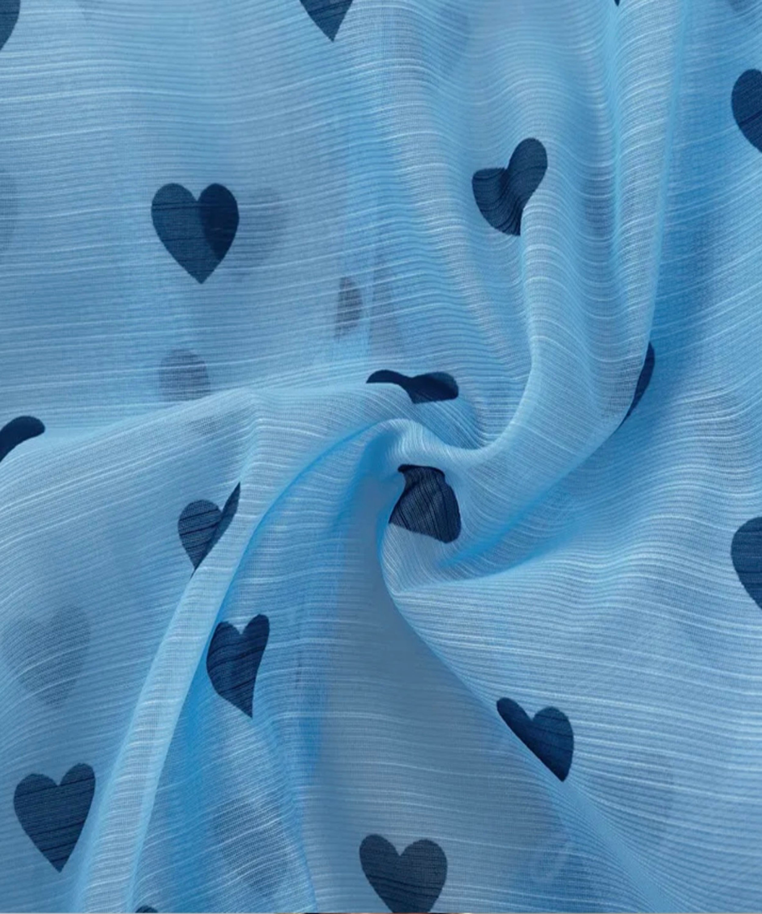 Light blue sheer fabric with a dark blue heart pattern, shown draped to display its texture and print.