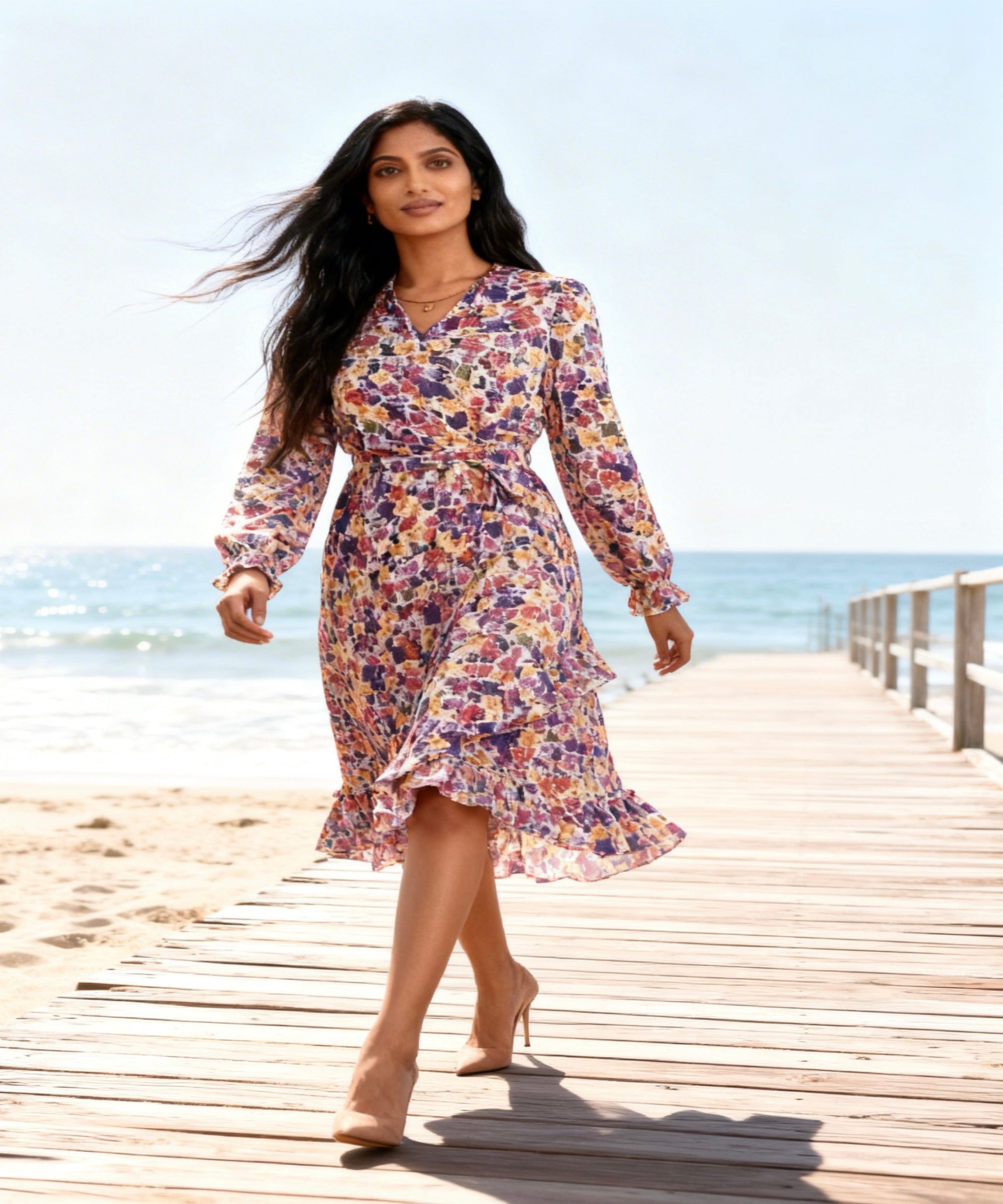 Woman in a floral dress walking on a wooden pier by the ocean.