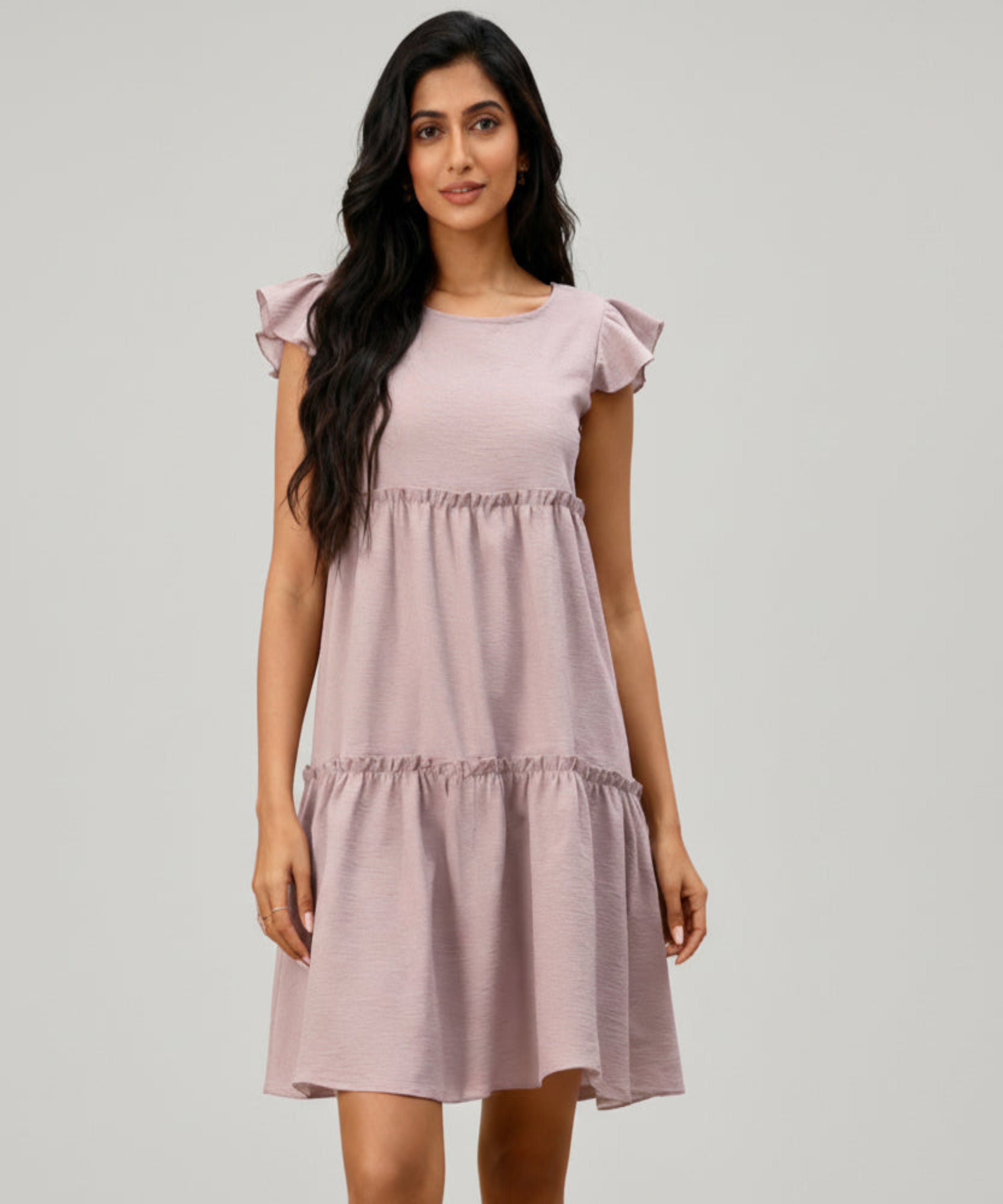 Woman wearing a light pink dress with ruffled sleeves on a white background