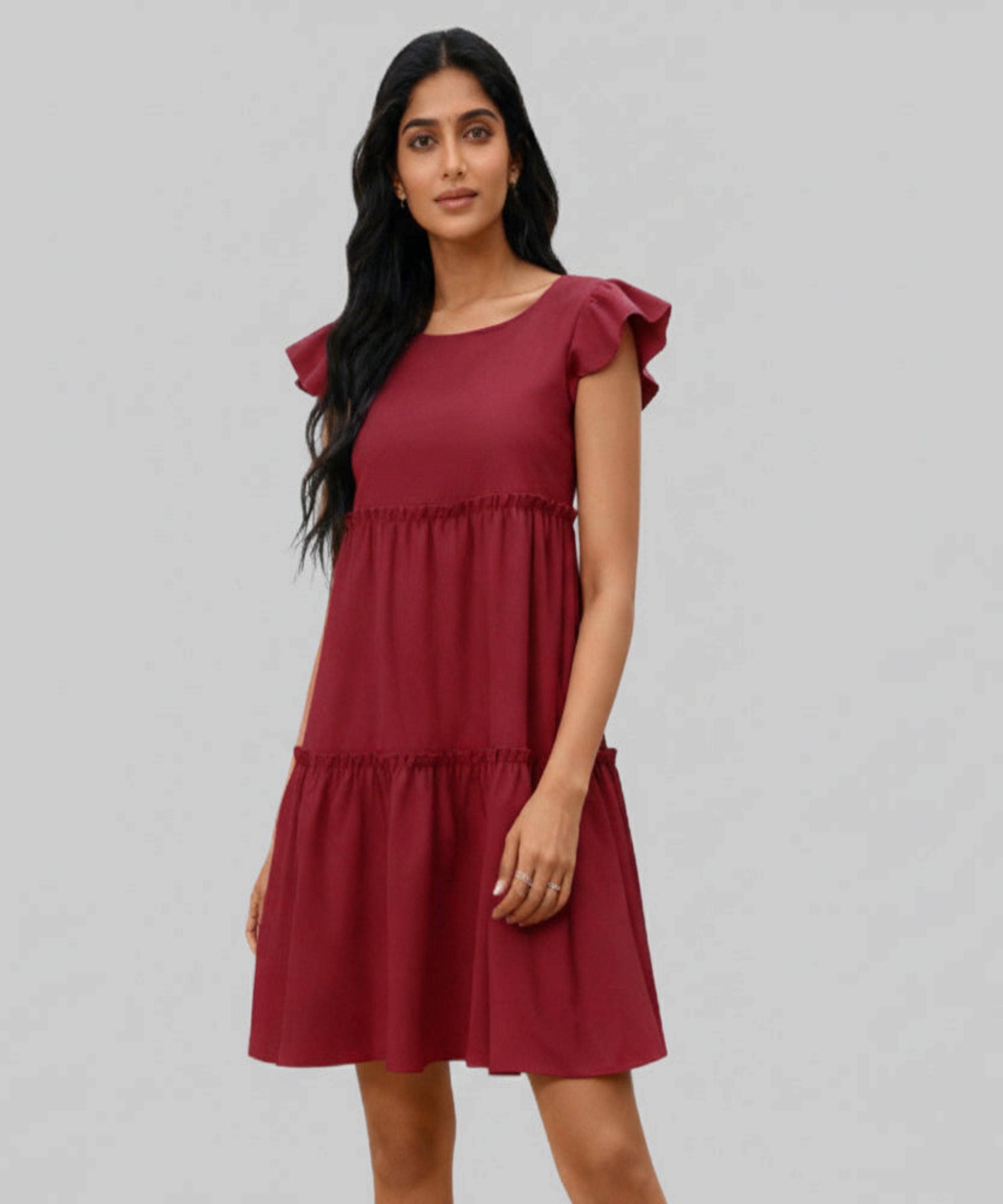 Woman wearing a burgundy dress with ruffled sleeves on a white background