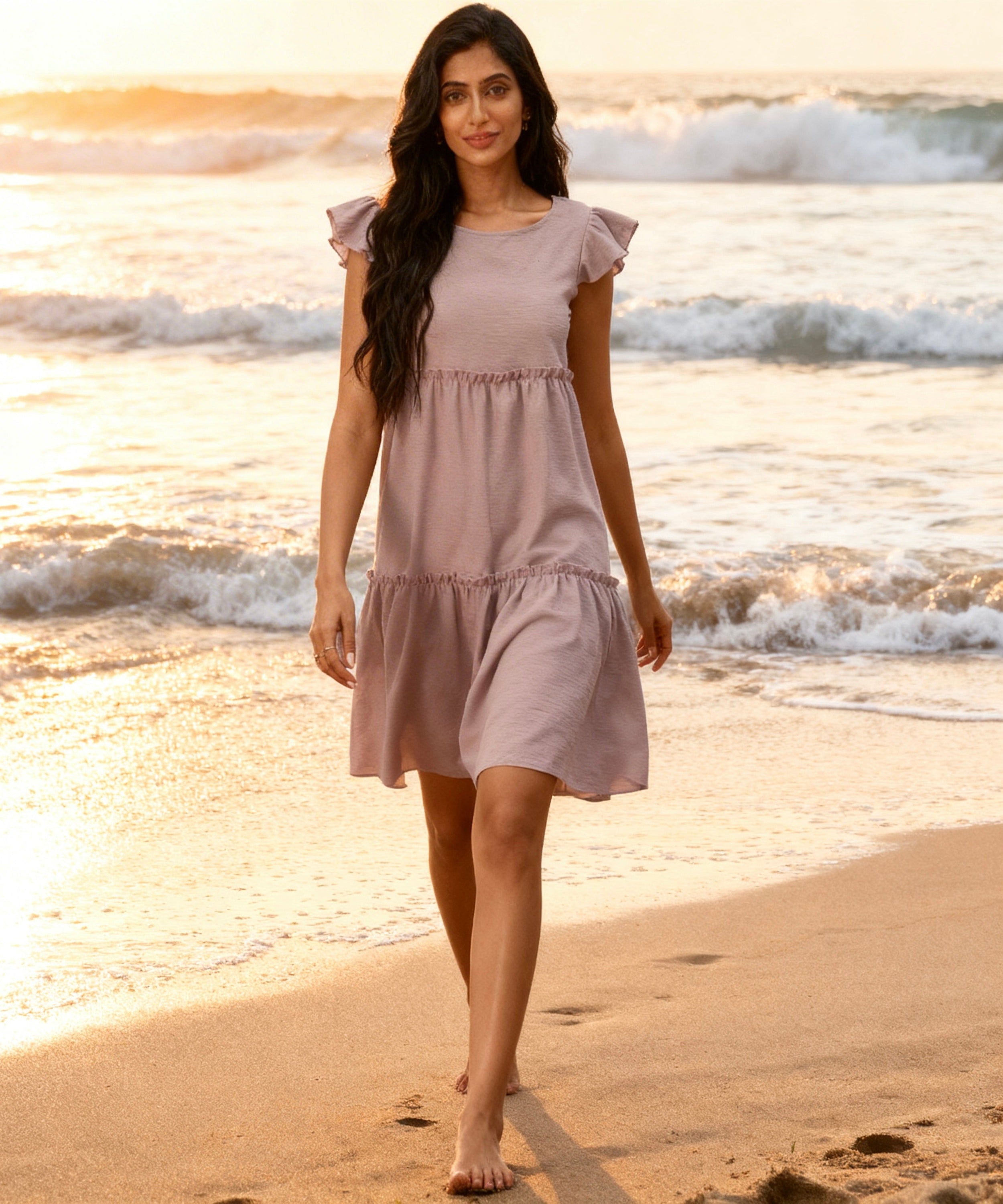 Woman in a light purple dress walking on a beach with waves in the background