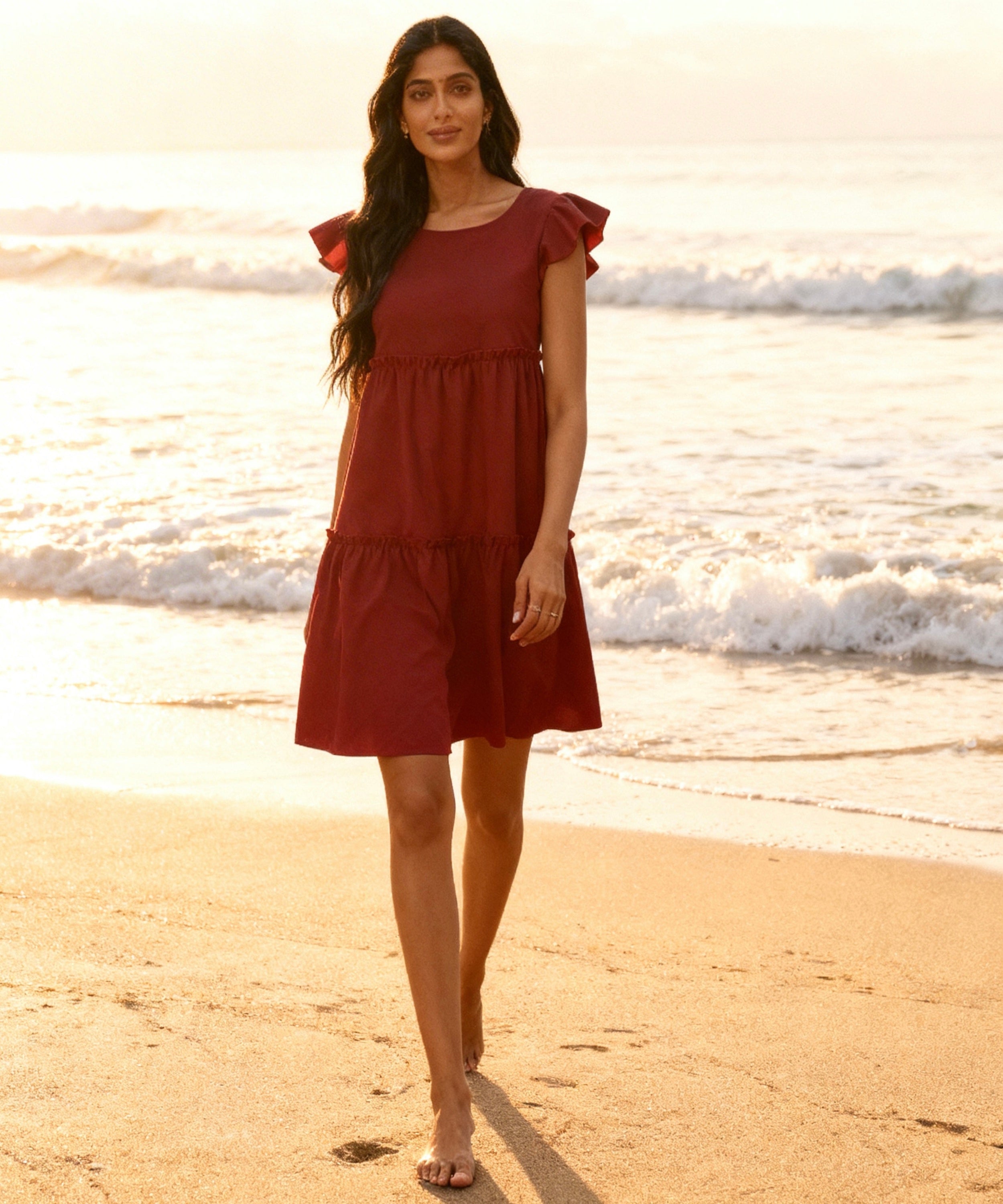 Woman in a red dress standing on a beach with waves in the background