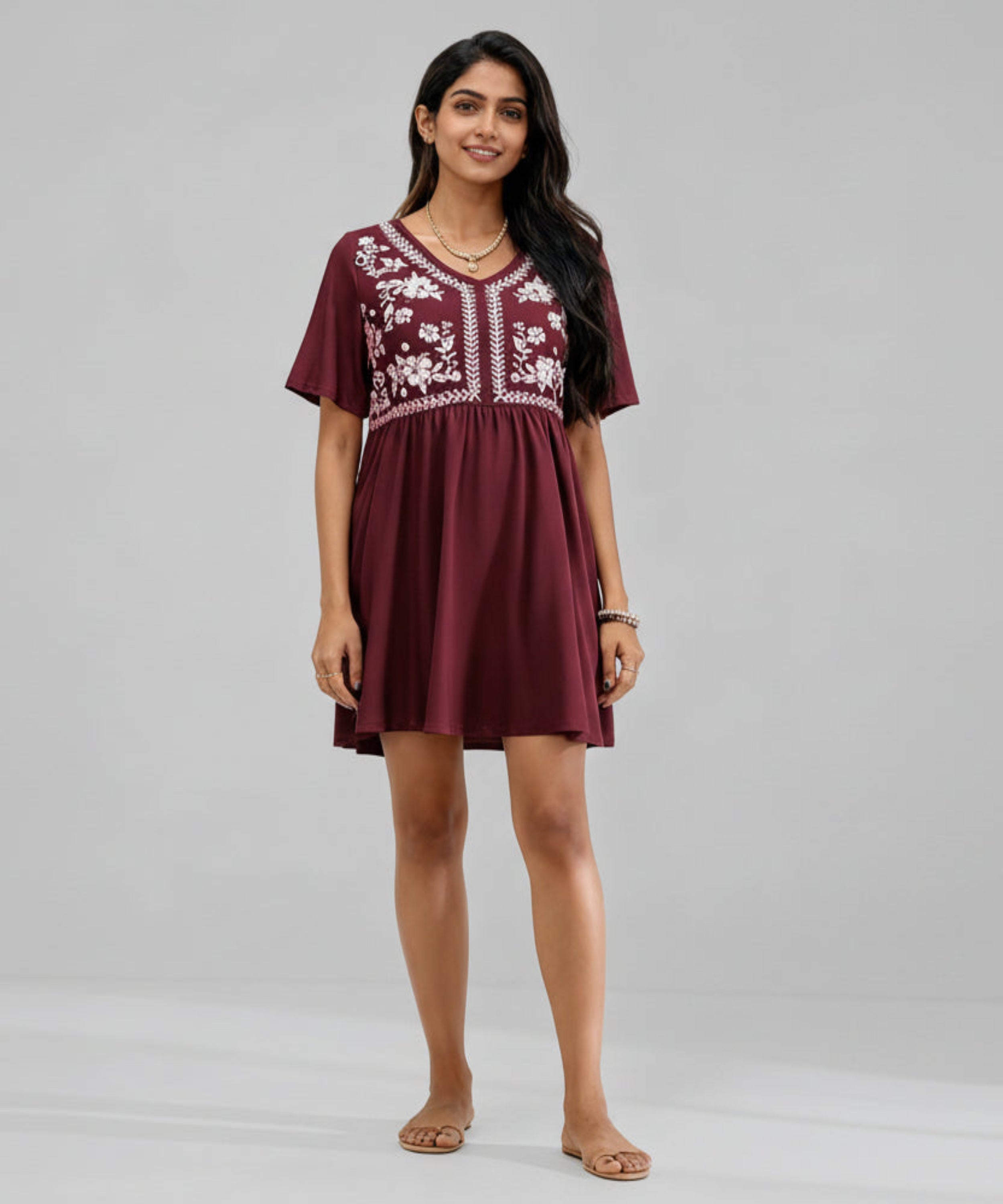 Woman wearing a maroon dress with white embroidery on a white background
