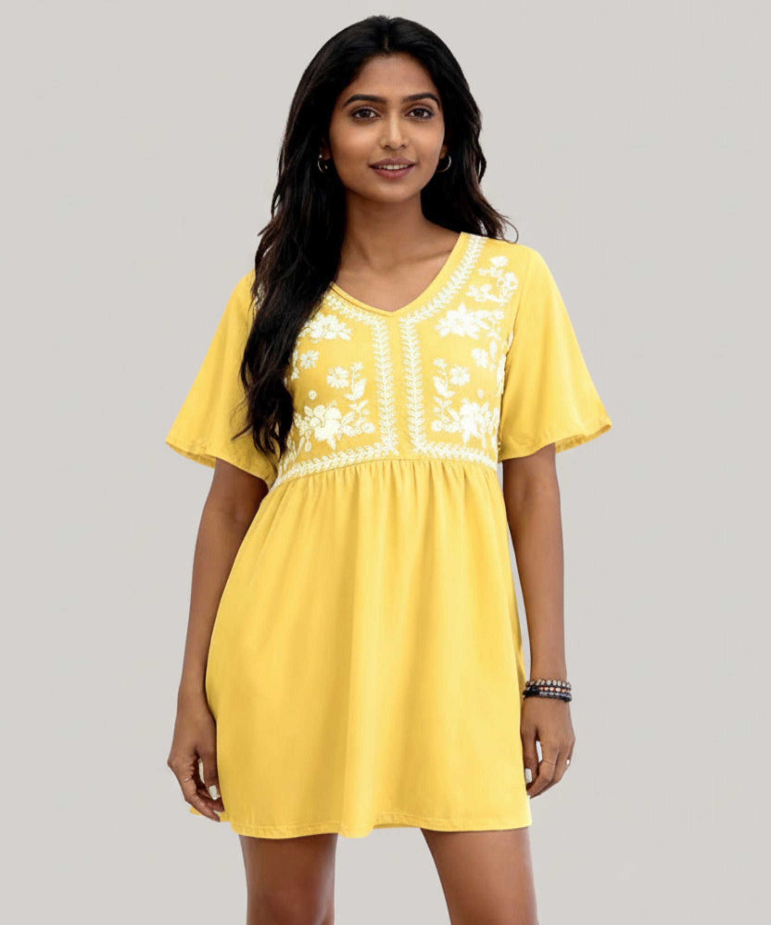 Woman wearing a yellow dress with white embroidery on a white background