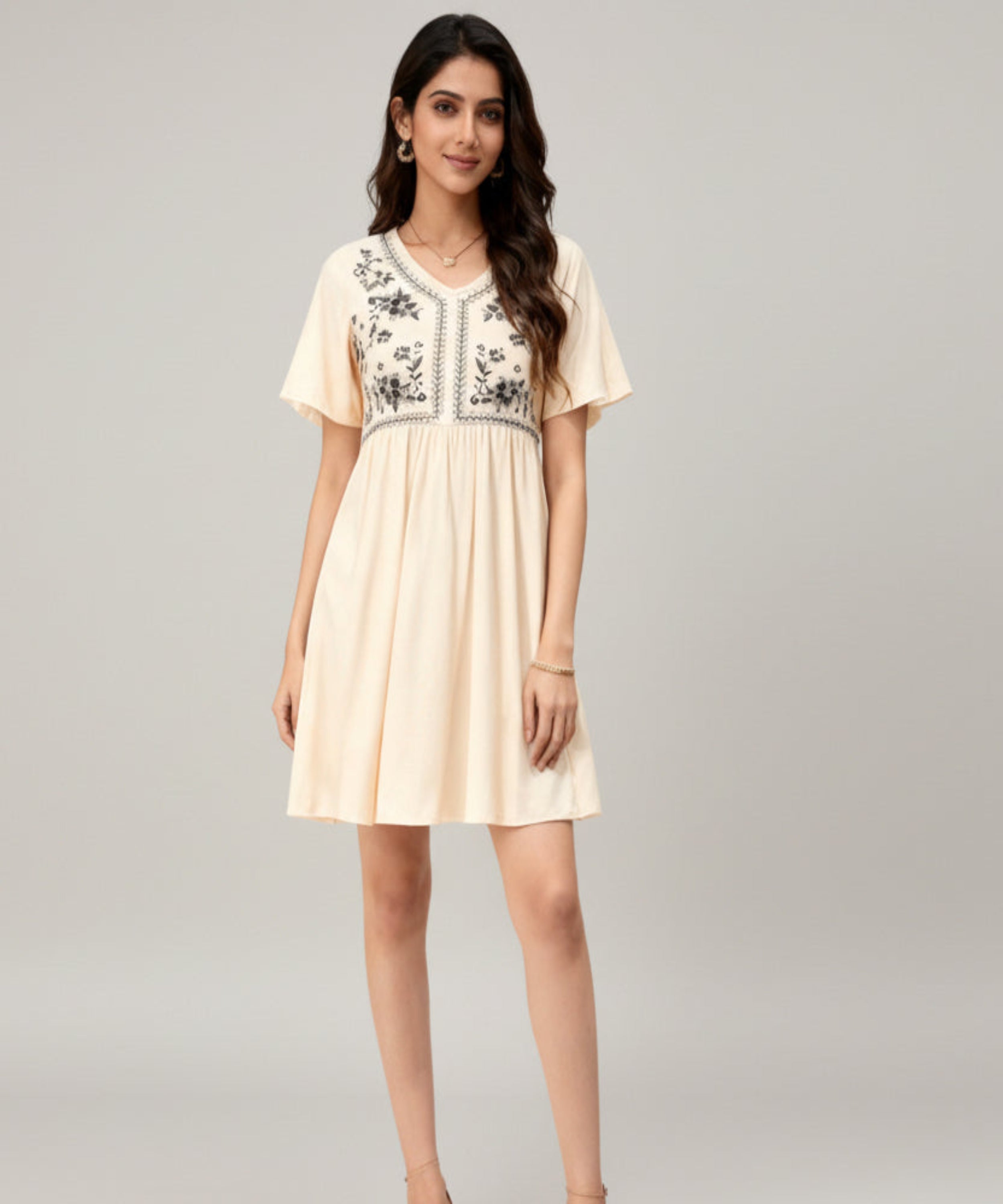 Woman wearing a beige dress with floral embroidery on a white background