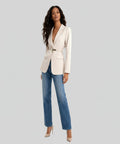 Woman wearing a white blazer and blue jeans on a white background