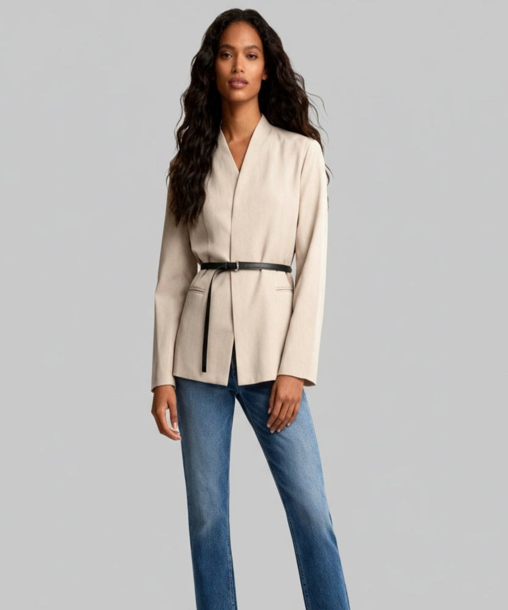 Woman wearing a beige blazer and blue jeans on a white background