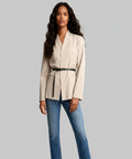 Woman wearing a beige blazer and blue jeans on a white background