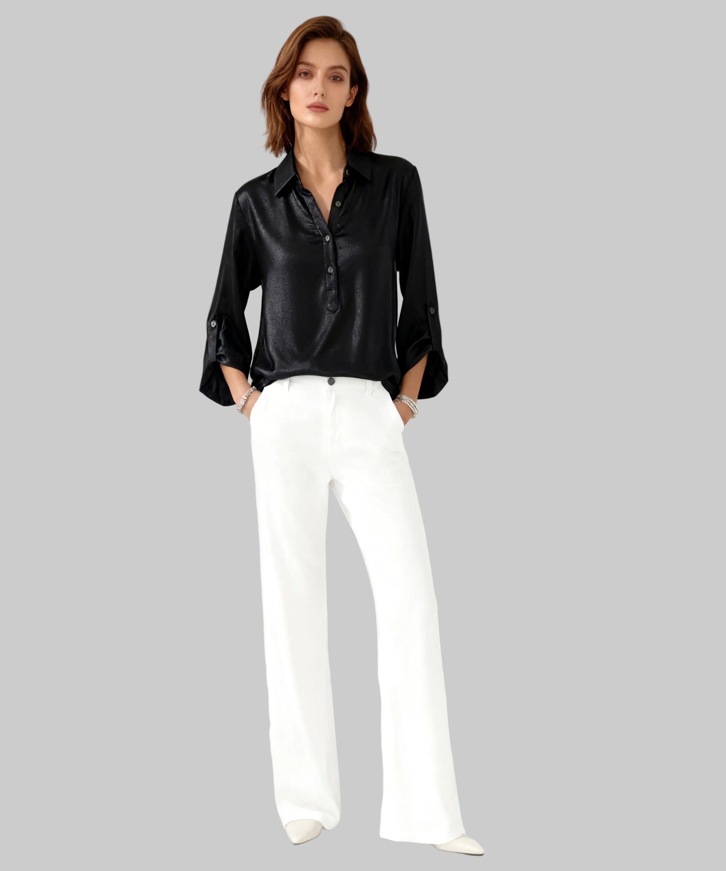 Woman wearing a black satin blouse and white pants on a white background