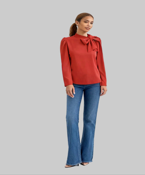 Woman wearing a red blouse with a bow detail and blue jeans on a white background