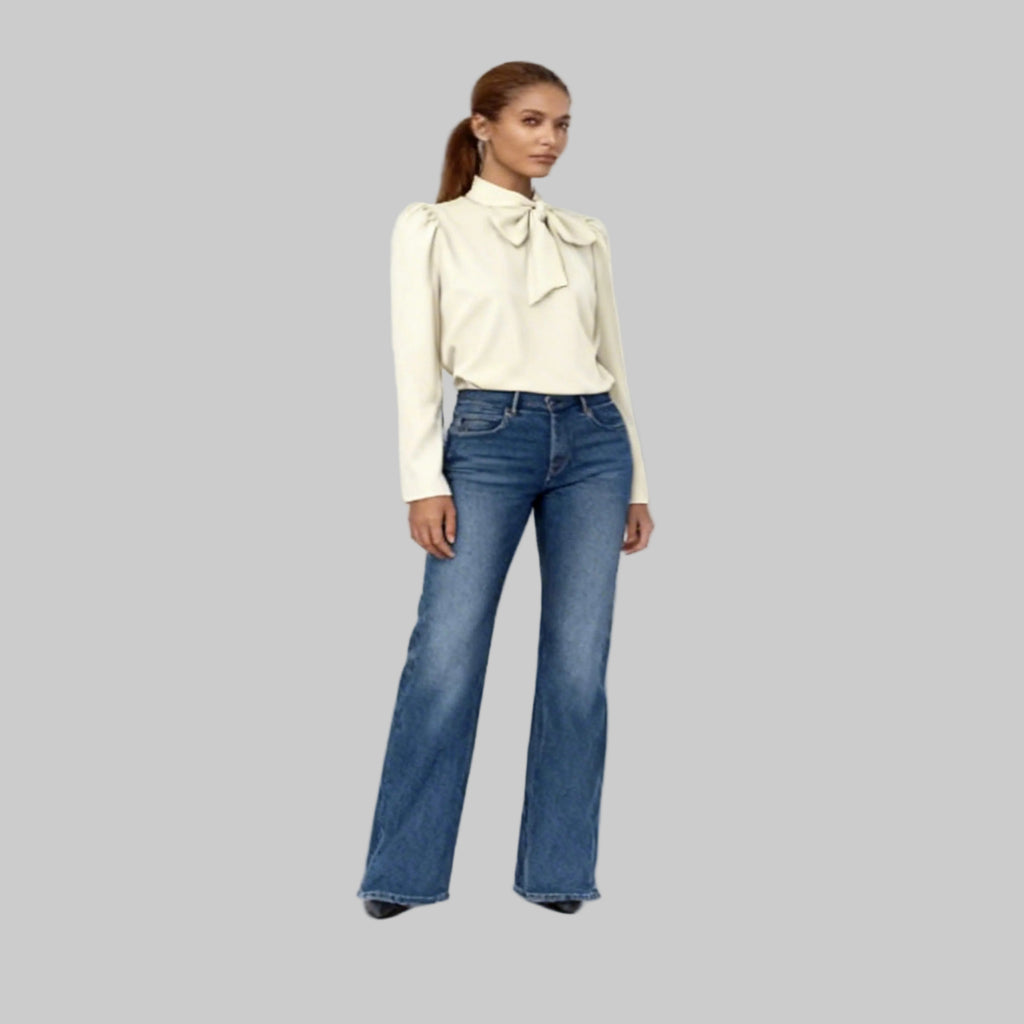 Woman wearing a cream blouse with a bow and blue jeans on a white background
