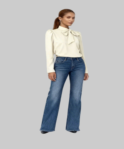 Woman wearing a cream blouse with a bow and blue jeans on a white background