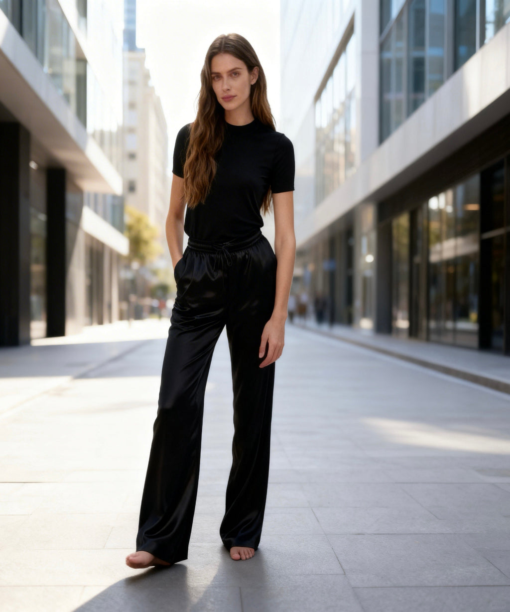 Woman in black outfit standing on a city street with modern buildings.