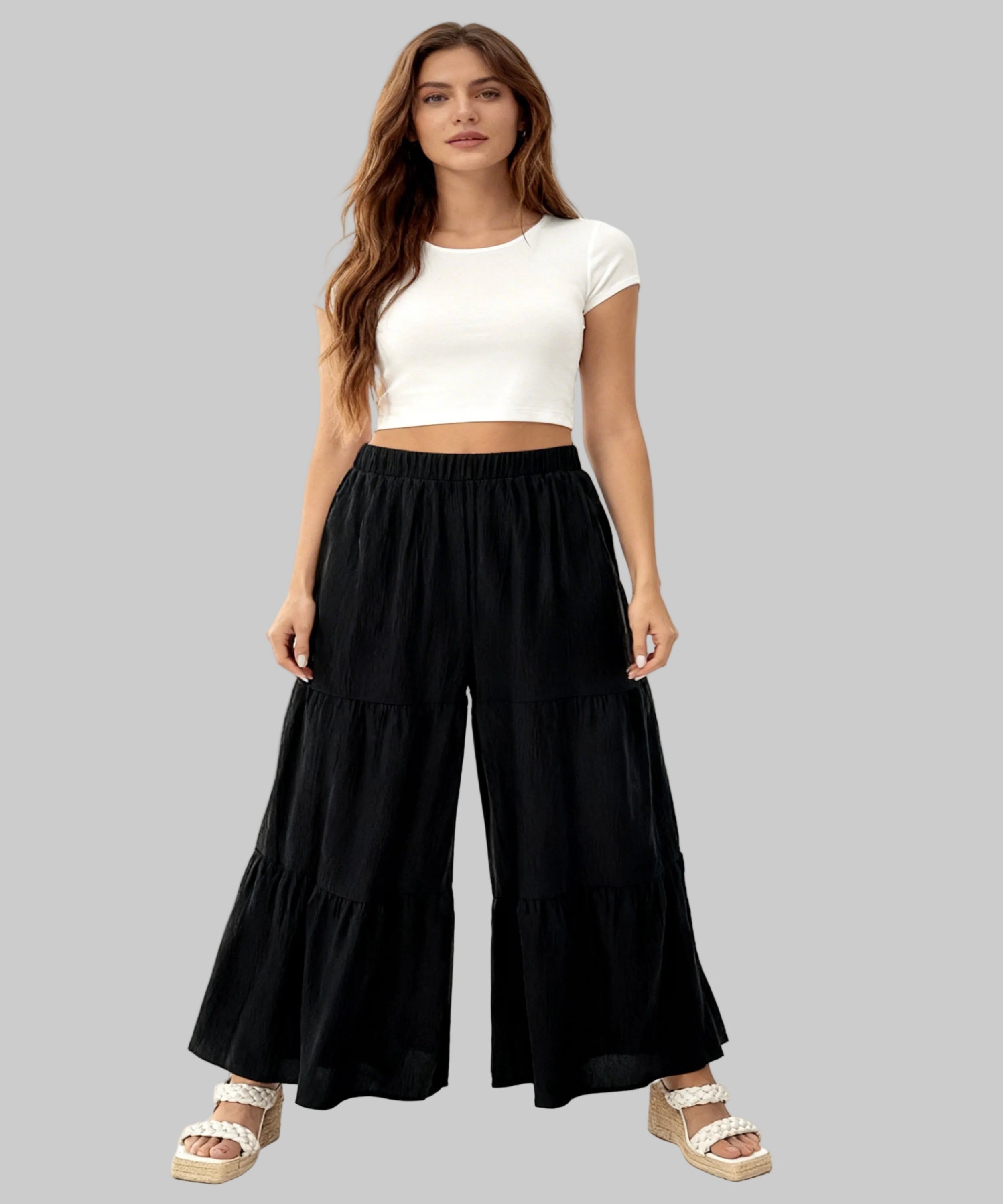 Woman wearing a white crop top and black wide-leg pants on a white background
