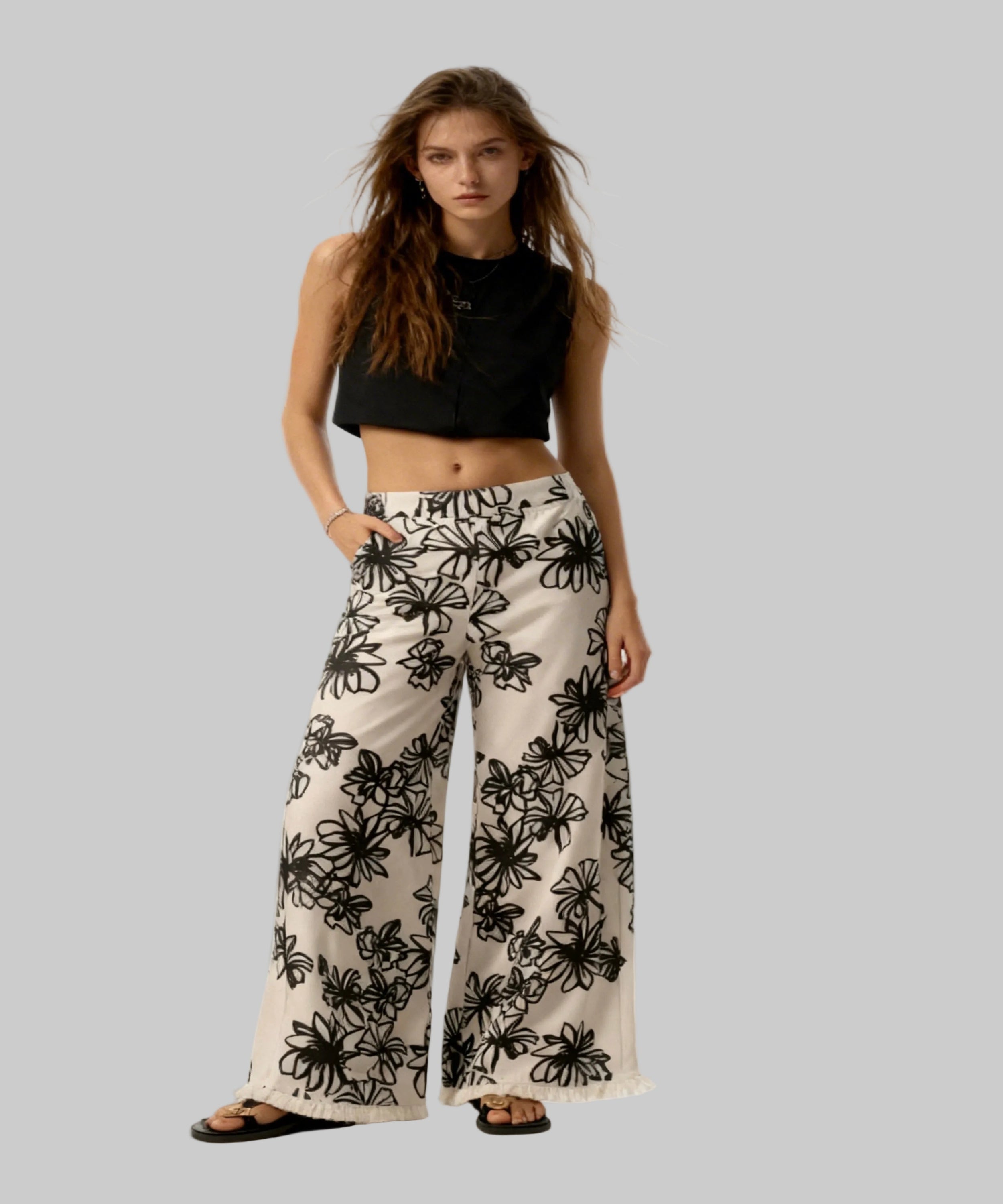 Woman wearing a black crop top and white pants with black floral patterns on a white background