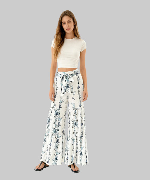 Woman wearing a white crop top and floral wide-leg pants on a white background
