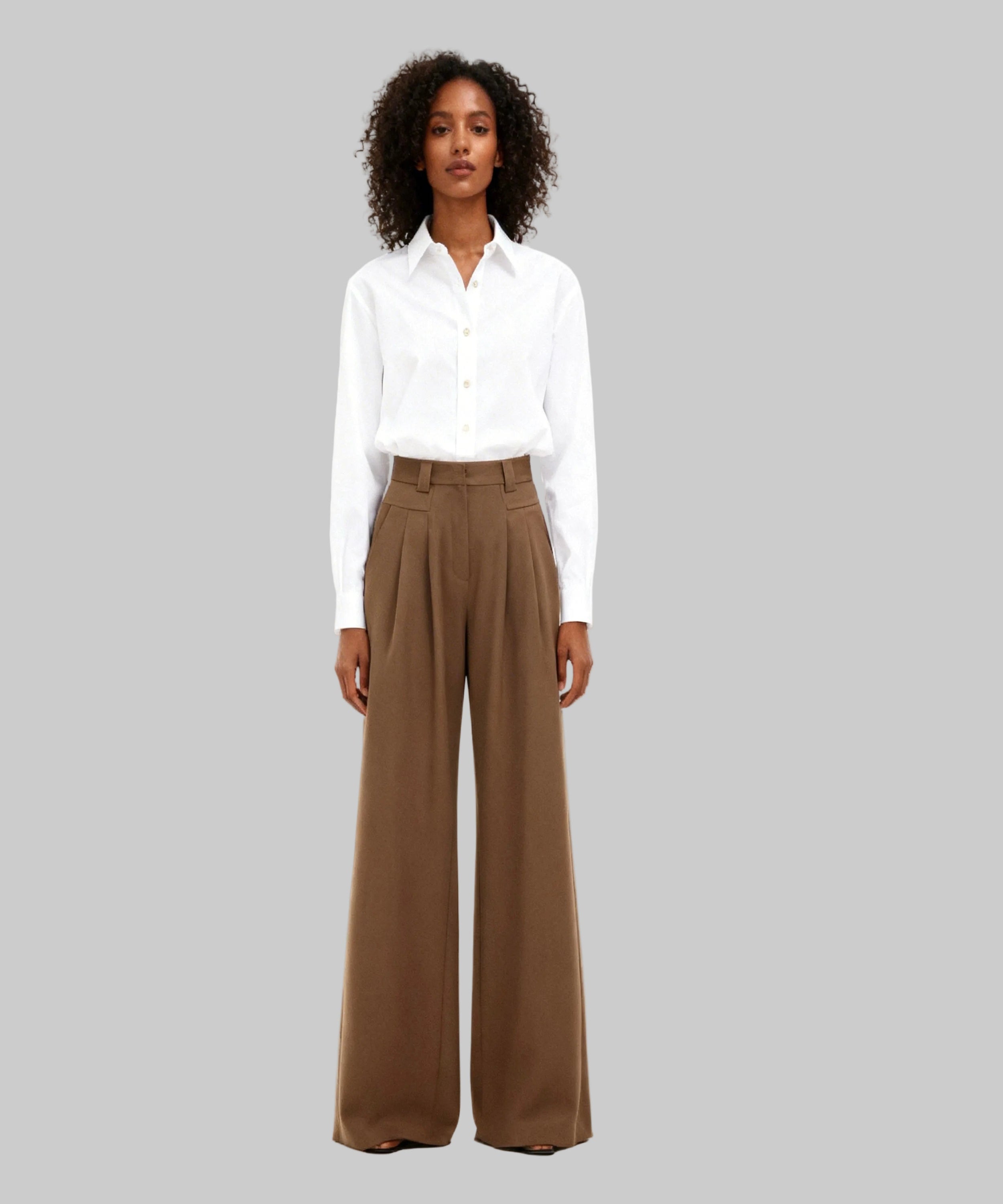 Woman wearing a white shirt and brown wide-leg pants on a white background