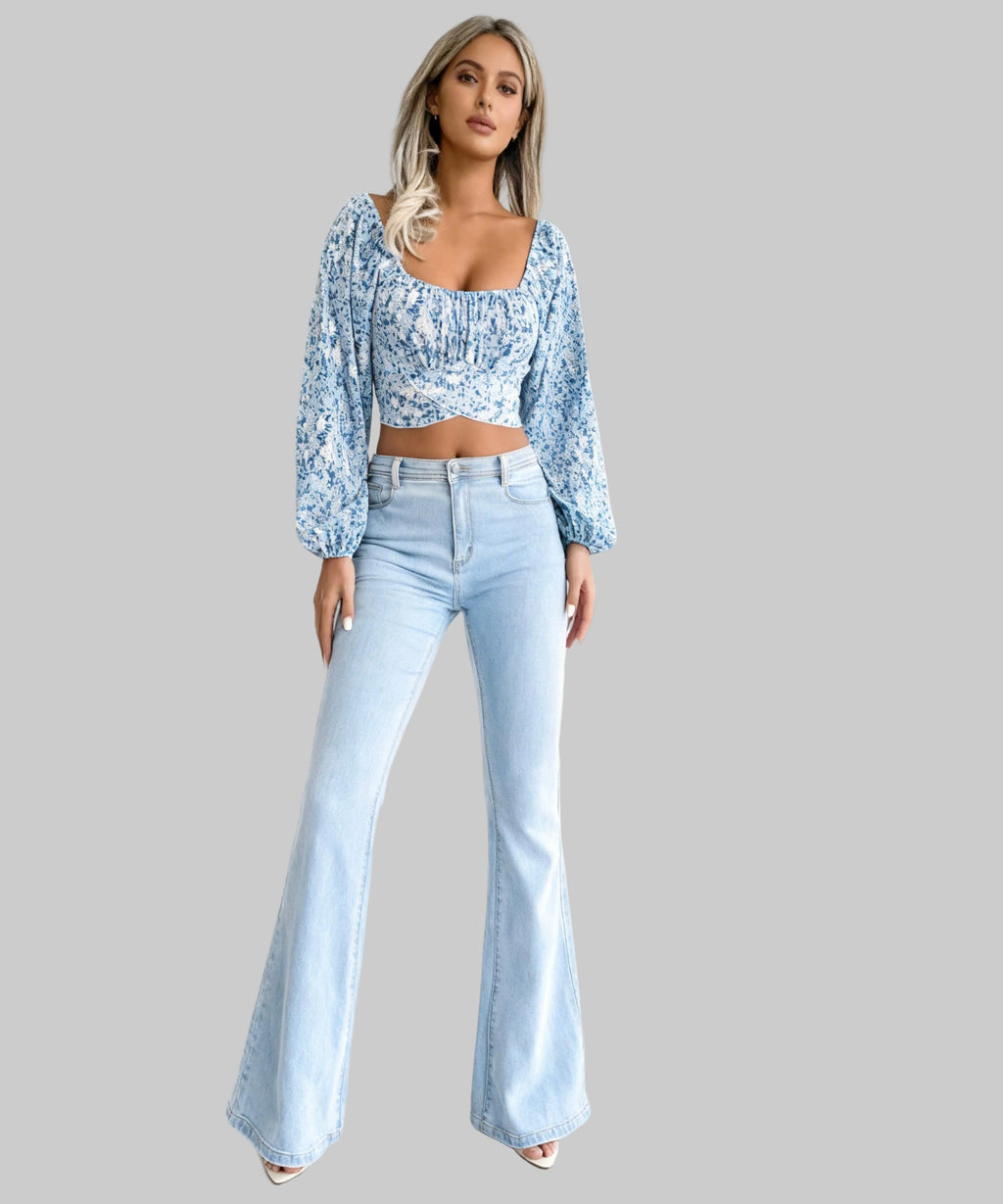 Woman wearing a floral top and light blue flared jeans on a white background