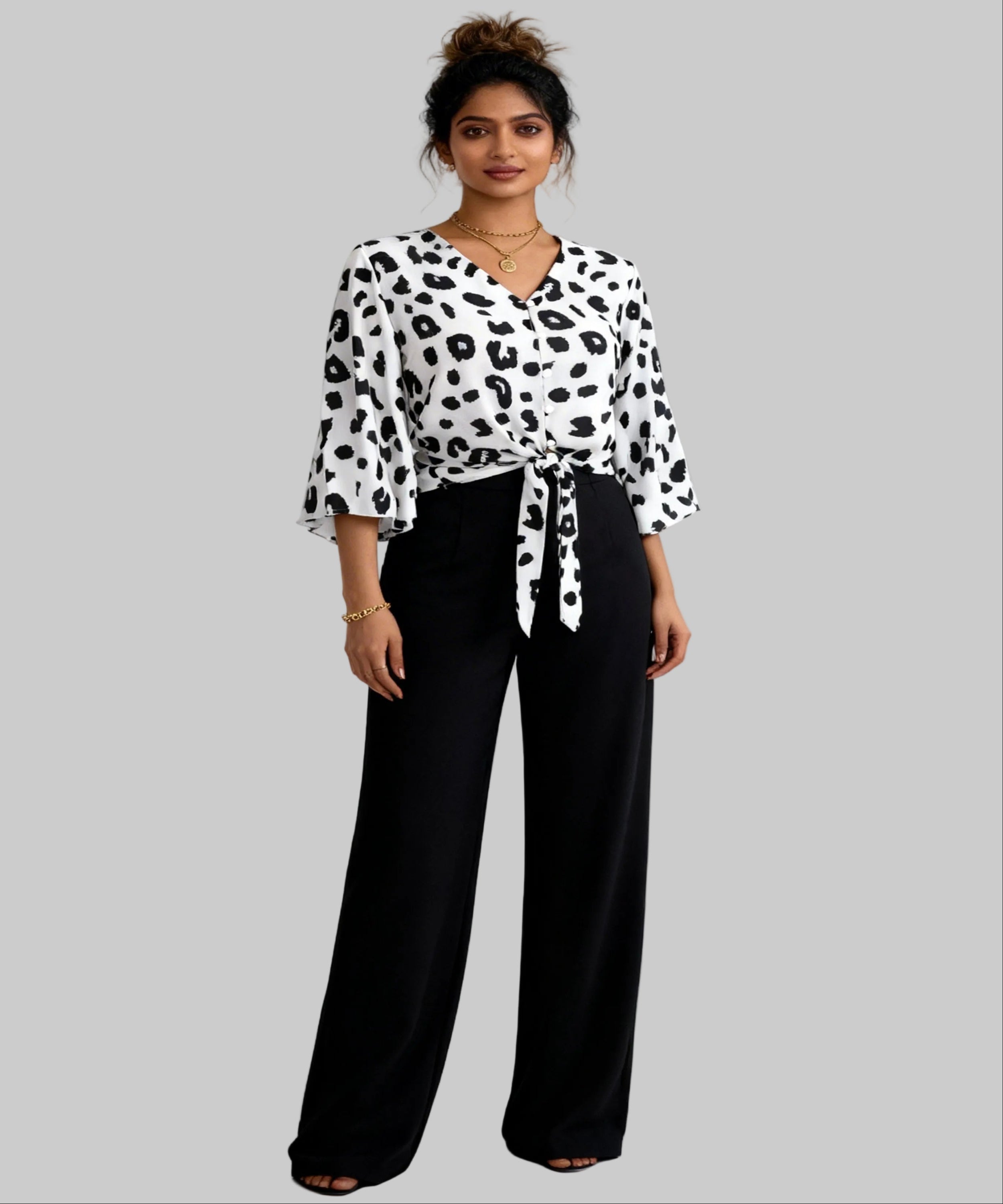 Woman wearing a black and white patterned blouse with black pants on a white background