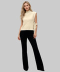 Woman wearing a cream sleeveless top with bow details and black pants on a white background