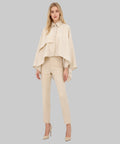 Woman wearing a beige outfit with a cape on a white background