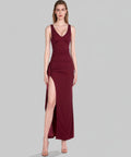 Woman wearing a burgundy evening gown with a slit on a light grey background