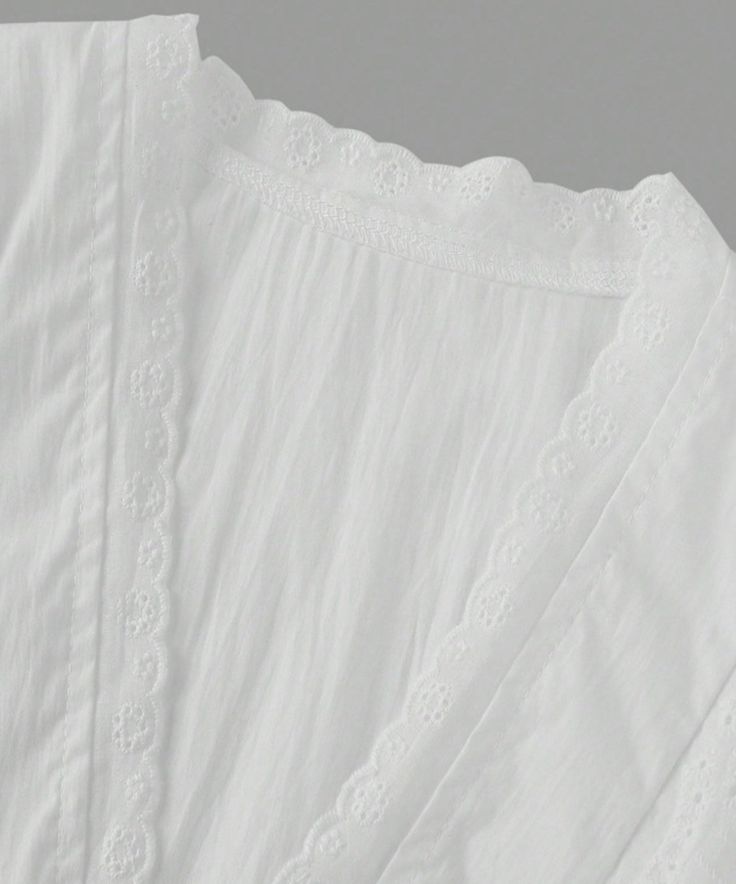 Close-up of a white textured fabric with lace detailing on a gray background