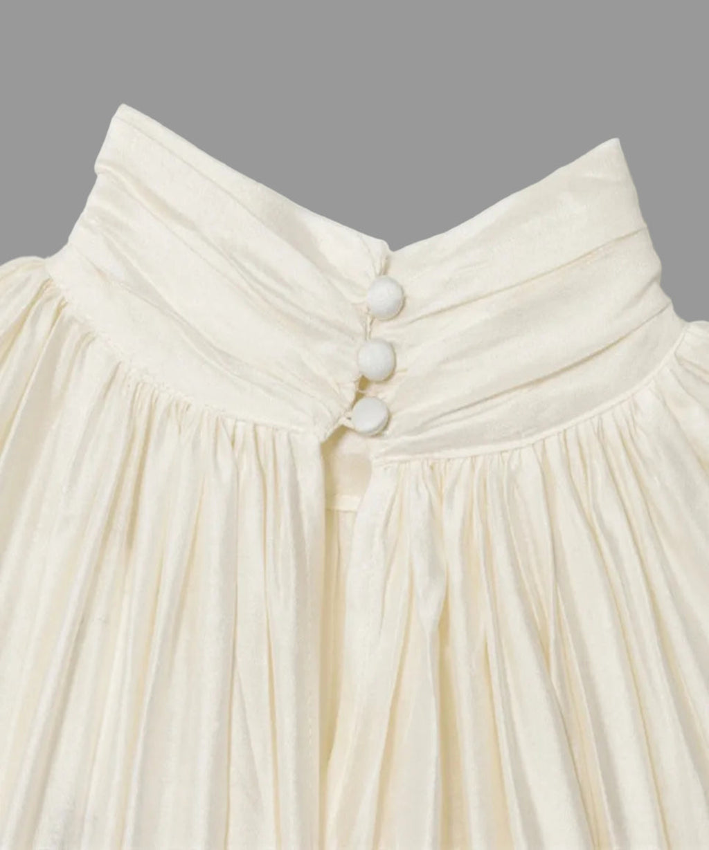Close-up of a cream-colored skirt with button details on a white background