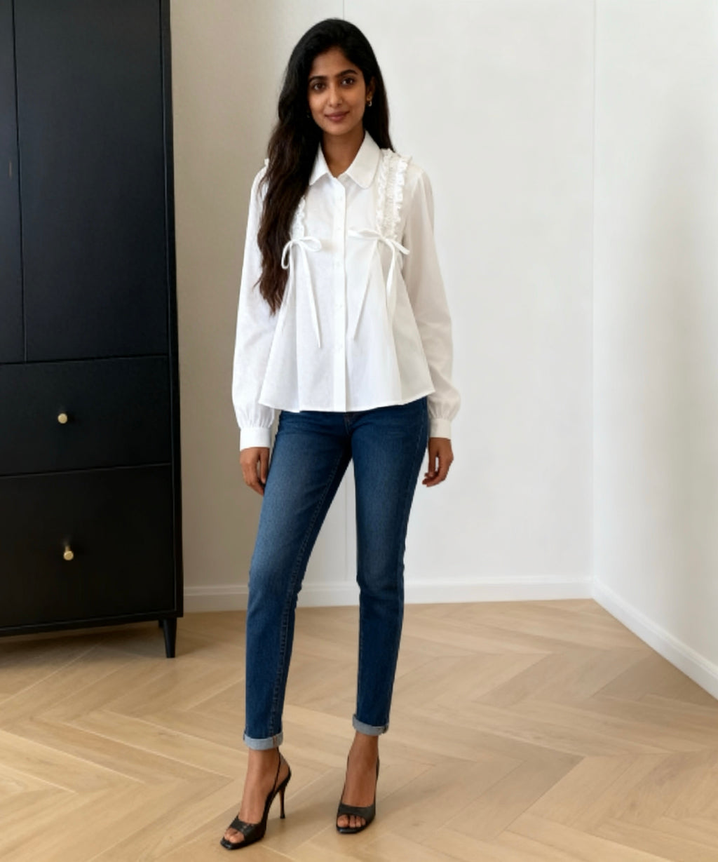 Woman wearing a white blouse and blue jeans standing in a room with a black cabinet and white wall.