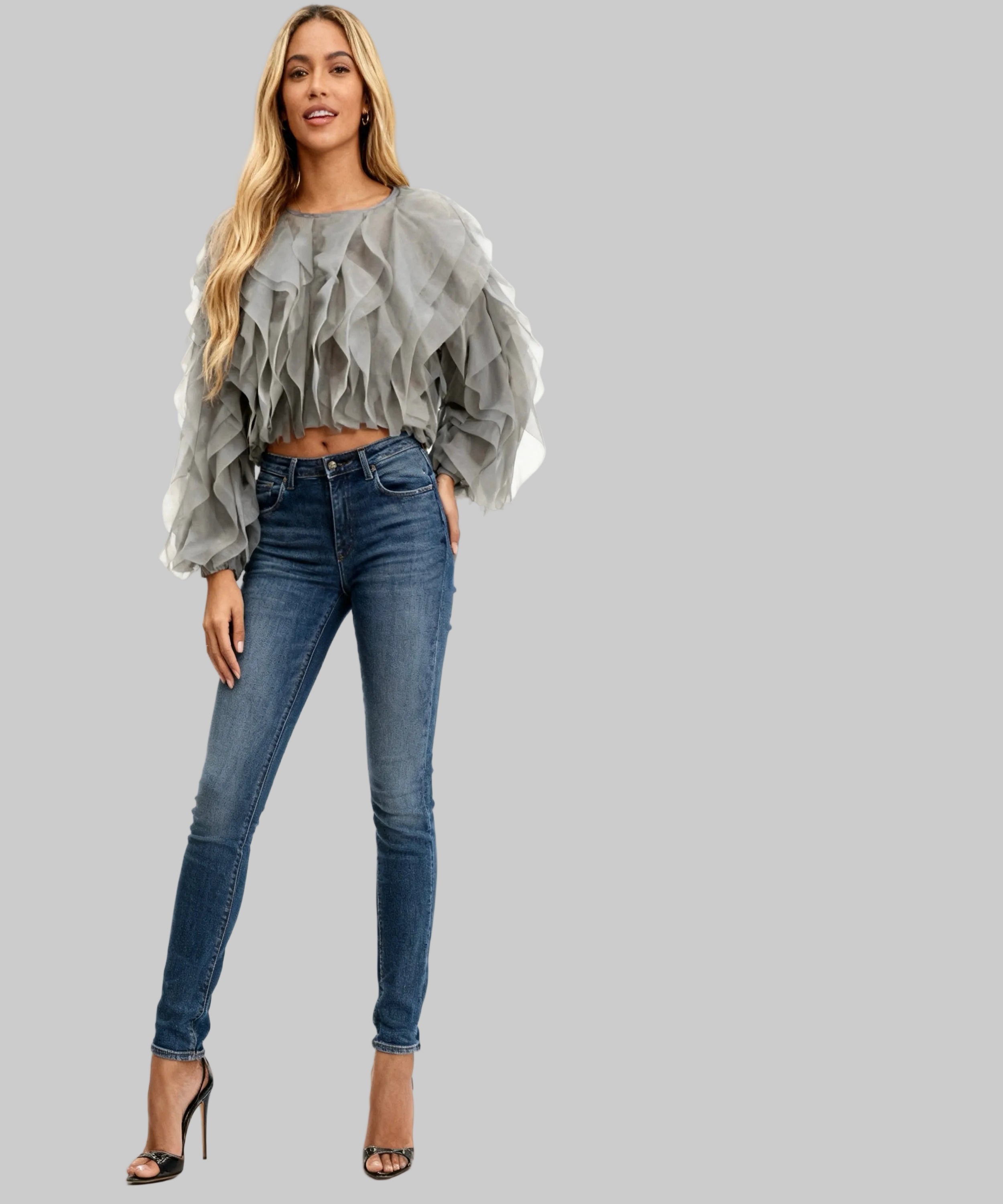 Woman wearing a gray ruffled blouse and blue jeans on a white background