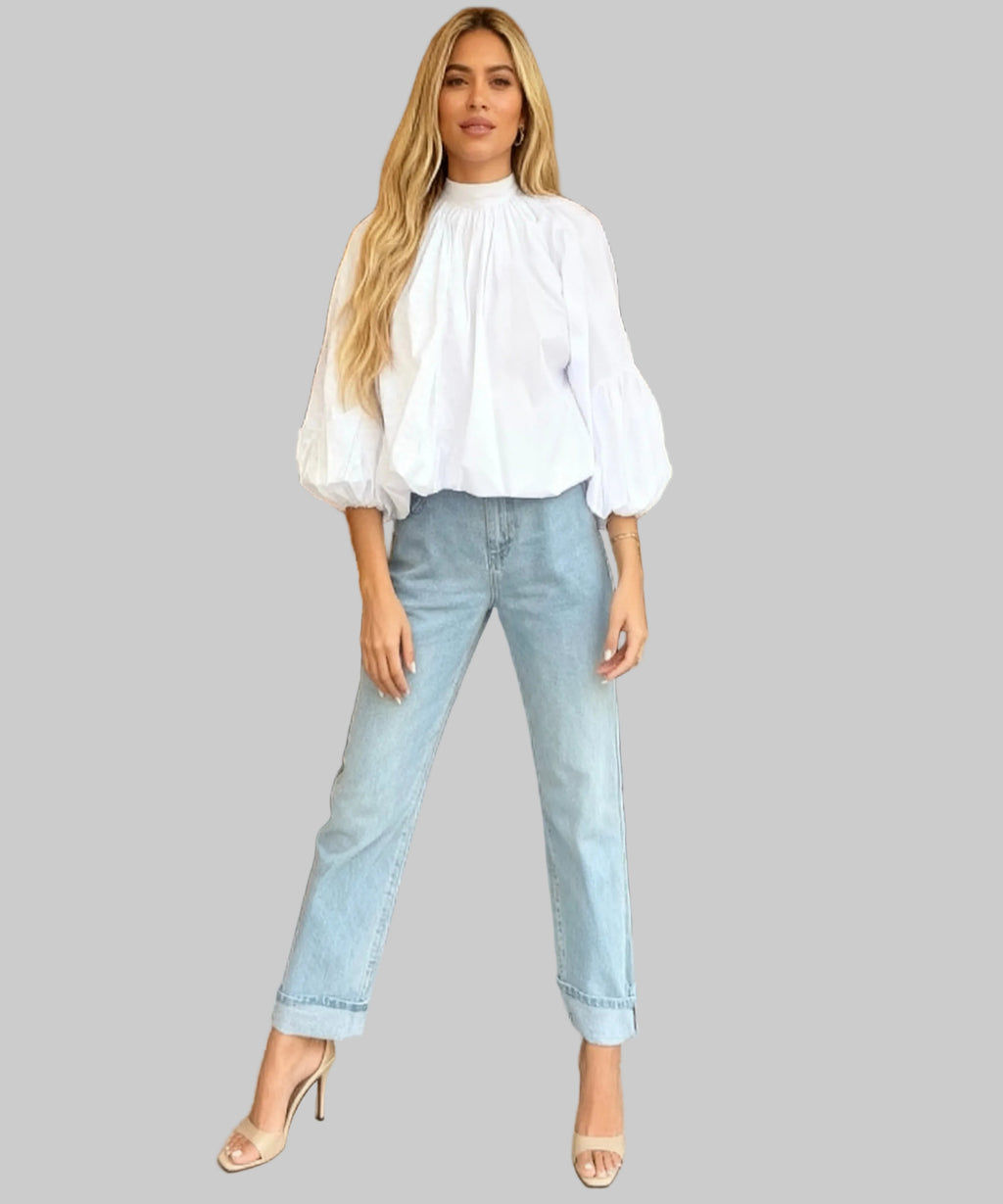 Woman in a white blouse and light blue jeans standing in a bakery.