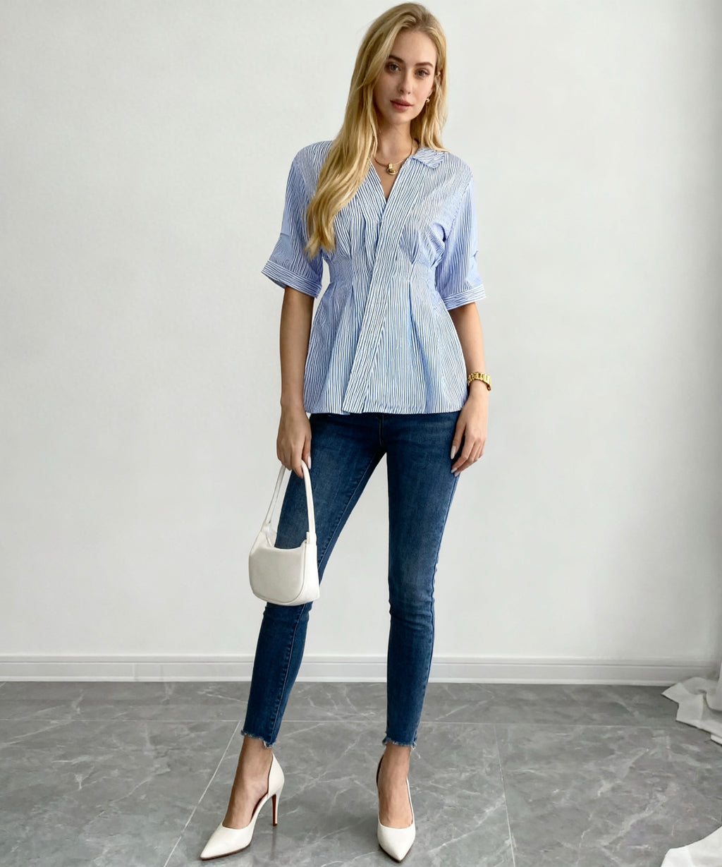 Woman wearing a blue checkered blouse and jeans, holding a white handbag against a plain background