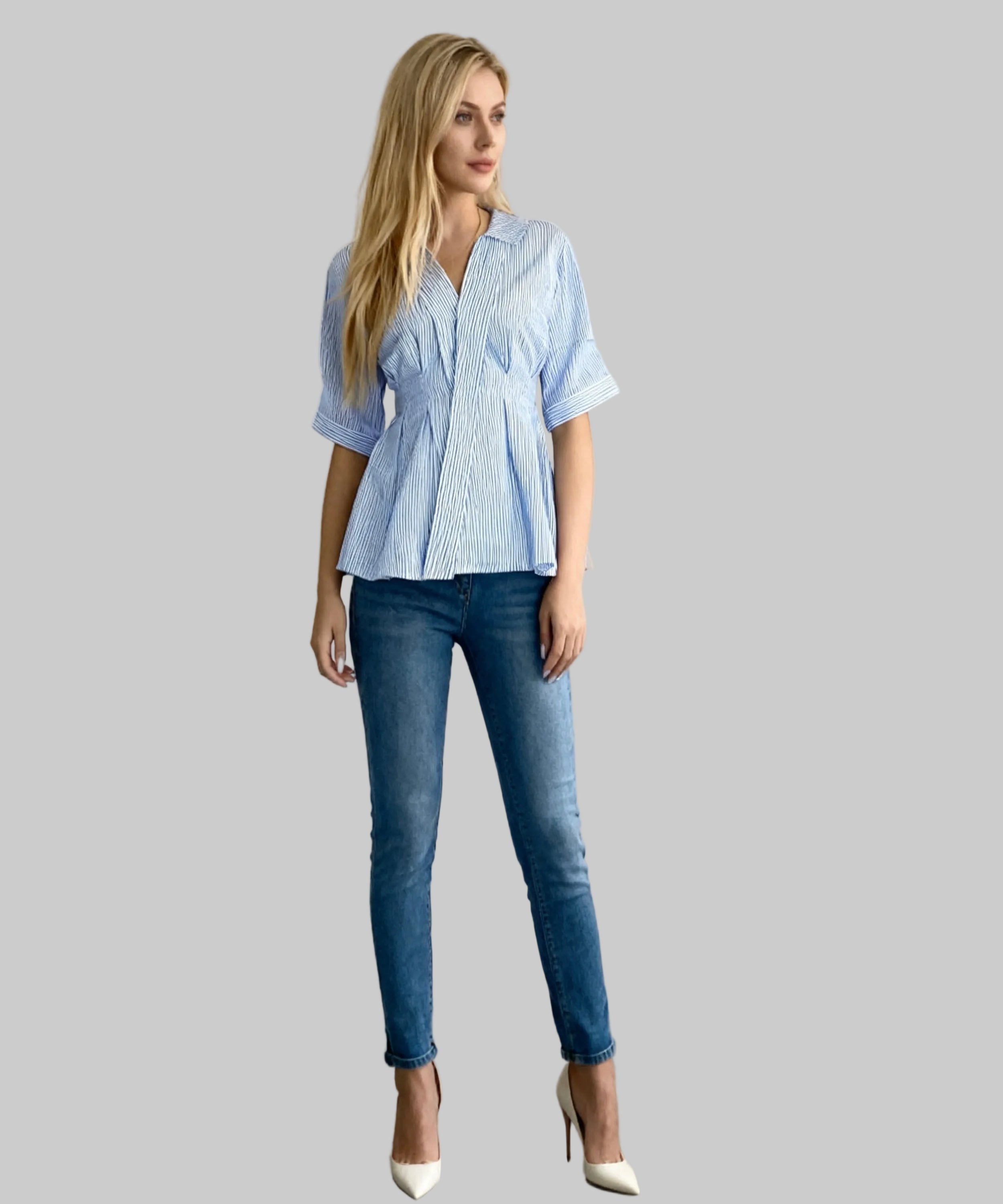 Woman wearing a light blue striped shirt and dark blue jeans against a plain background