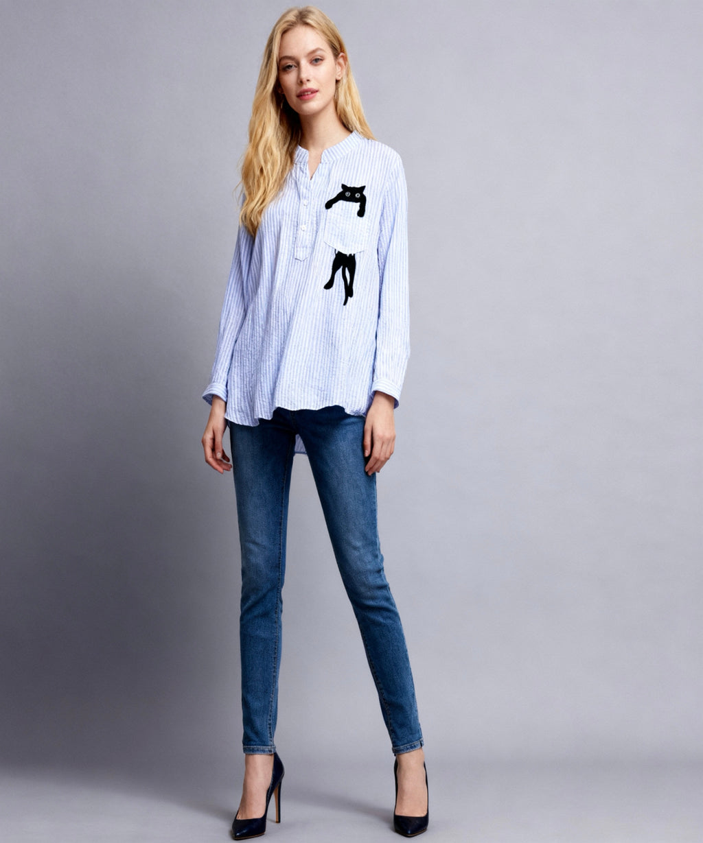 Woman wearing a light blue shirt with black cat illustrations and blue jeans on a gray background