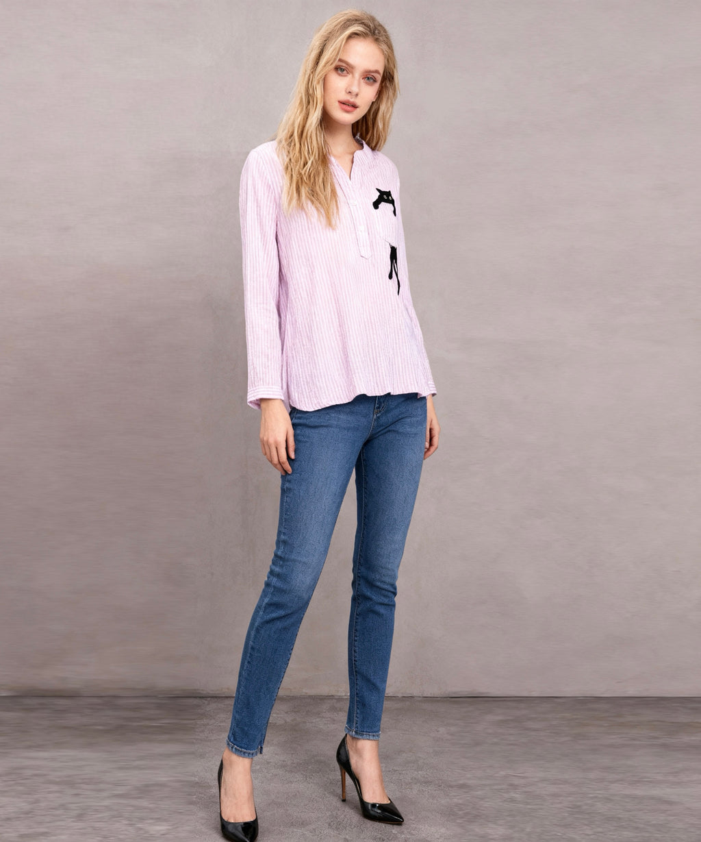 Woman wearing a light purple blouse with black designs and blue jeans against a gray background