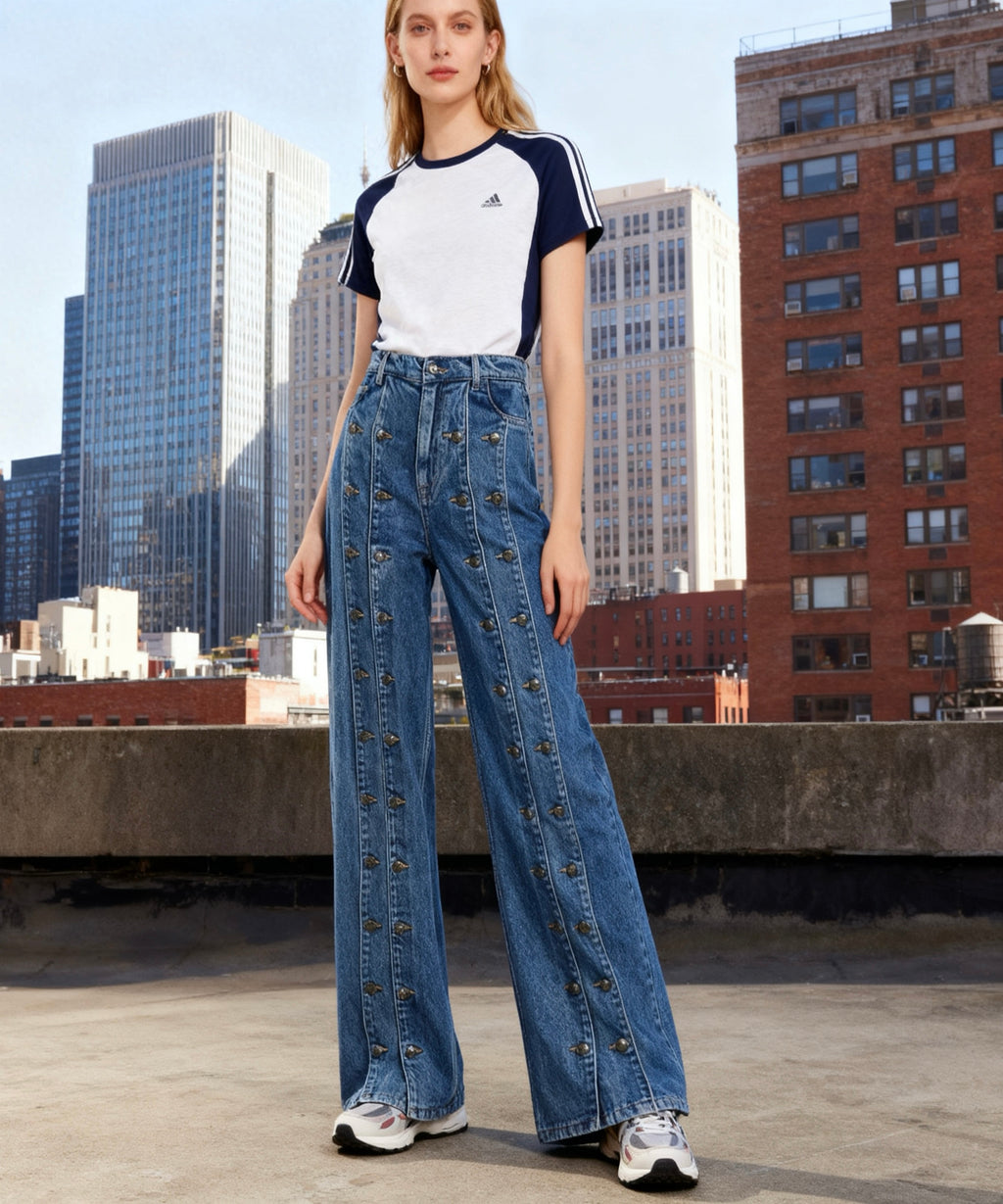 Woman wearing an Adidas t-shirt and denim pants on a rooftop with cityscape background
