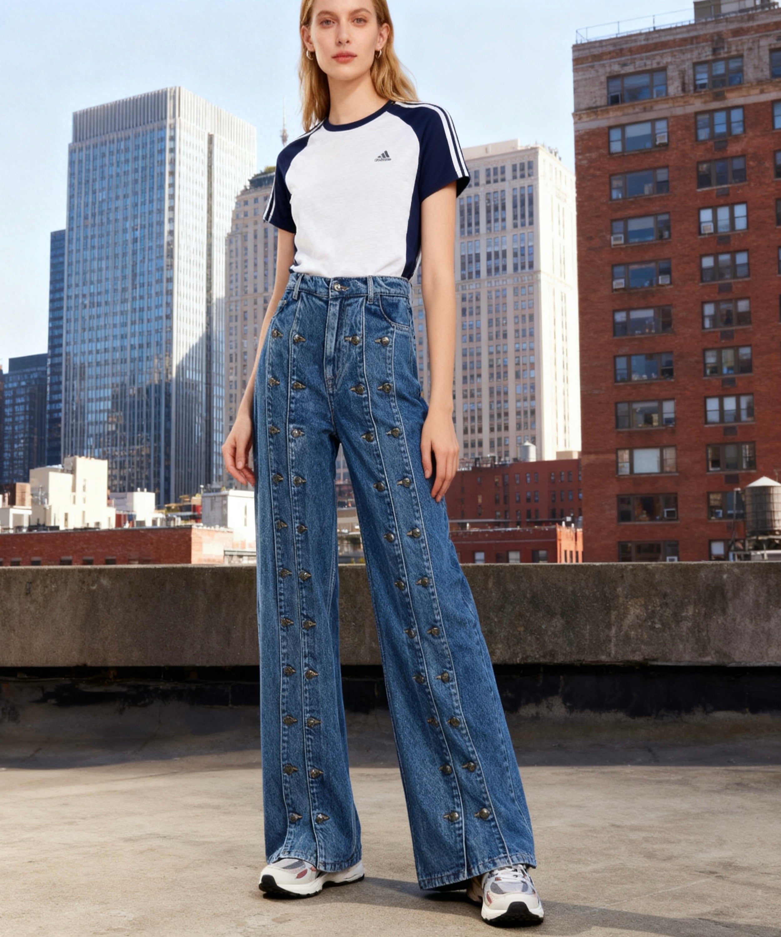 Woman wearing an Adidas t-shirt and denim pants on a rooftop with cityscape background