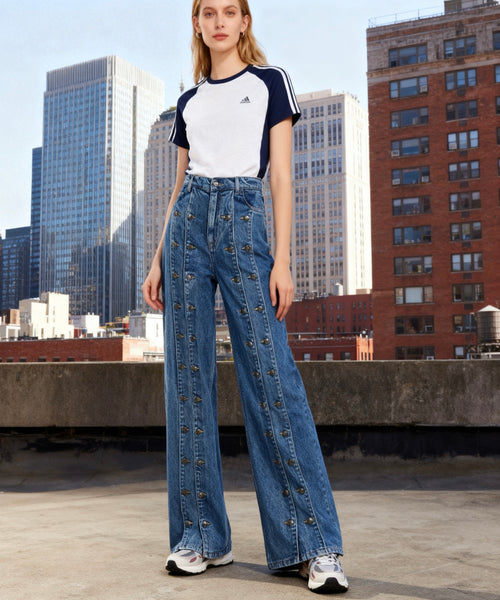 Woman wearing an Adidas t-shirt and denim pants on a rooftop with cityscape background