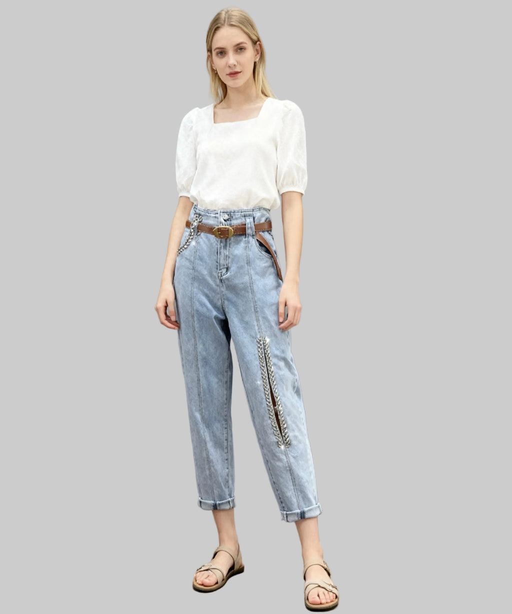 Woman wearing a white blouse and light blue jeans with decorative zippers against a gray background