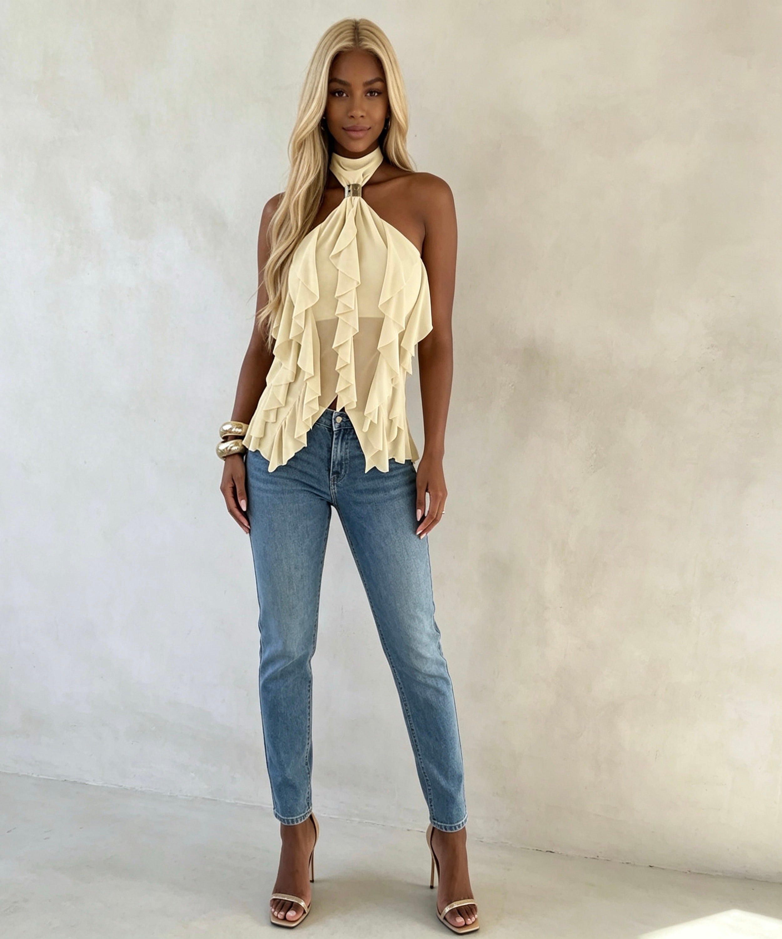 Woman wearing a beige halter top and blue jeans against a plain background