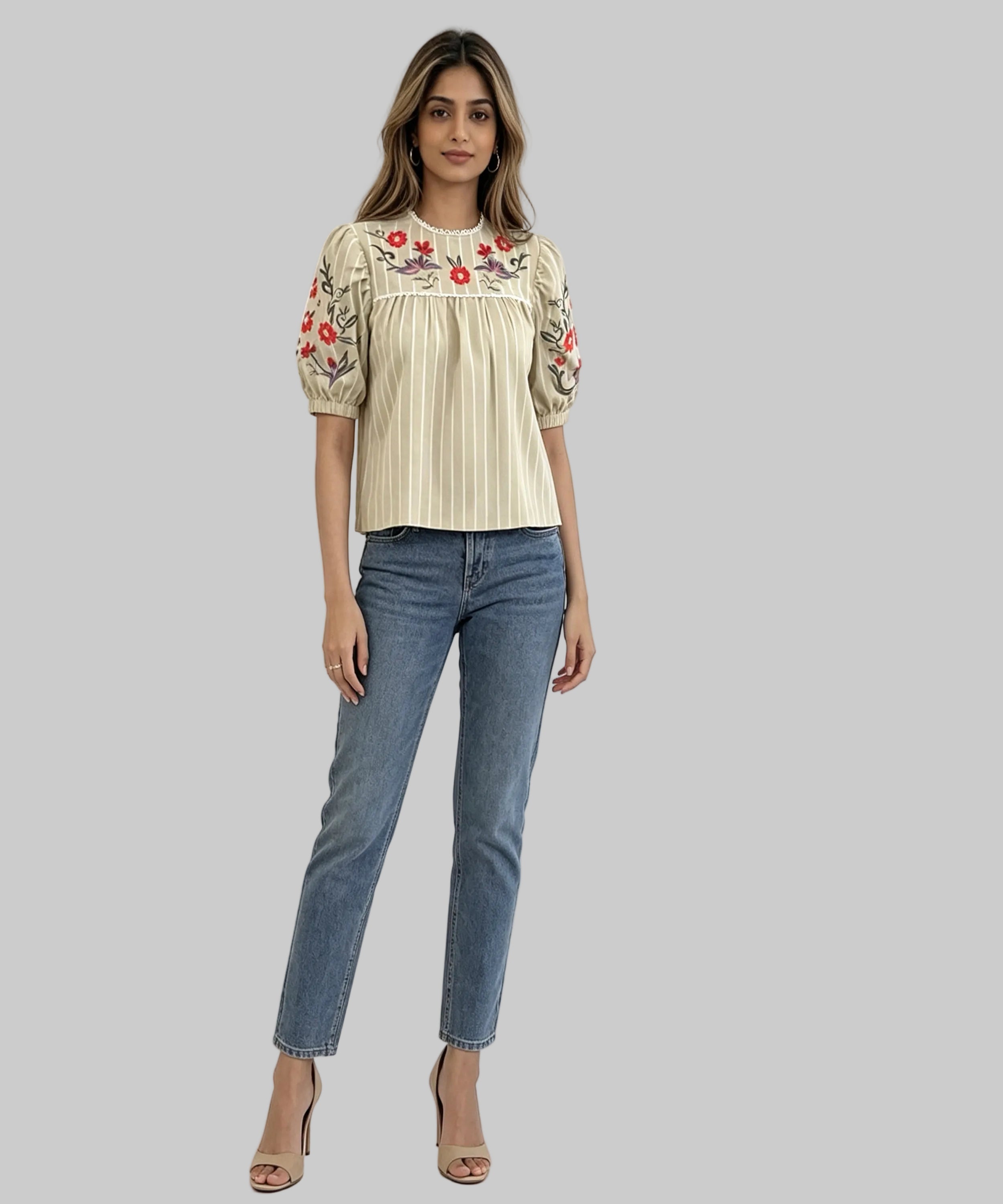Woman wearing a cream blouse with floral embroidery and blue jeans on a white background