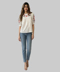 Woman wearing a white blouse with floral embroidery and blue jeans on a white background