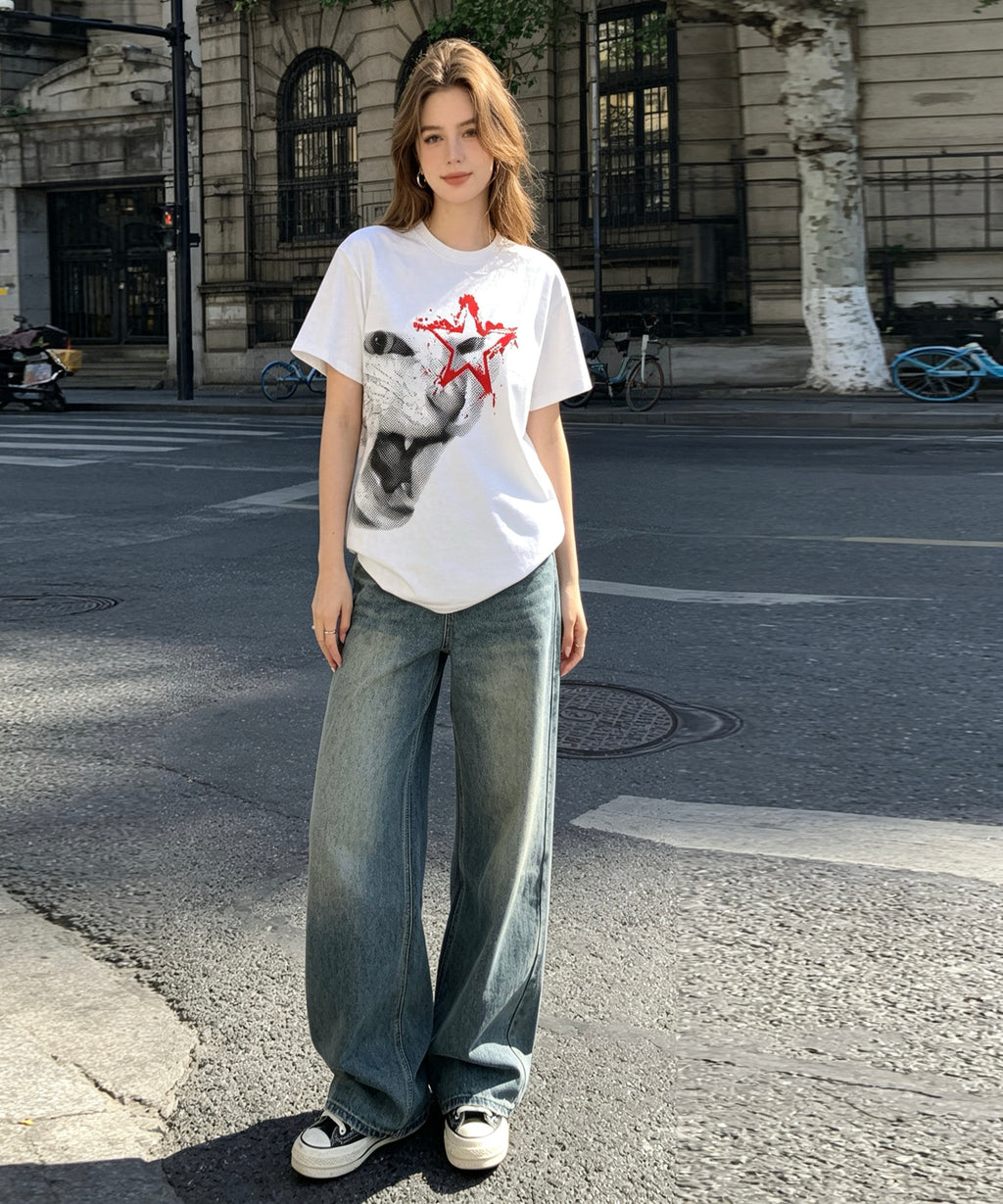 Woman wearing a white t-shirt with a graphic design and blue jeans standing on a street.