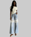 Woman wearing light blue jeans with lace details and a white top against a plain background
