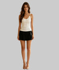 Woman standing on a balcony wearing a white top and black shorts.