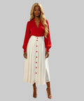 Woman in a red blouse and white skirt with red buttons standing on a white background