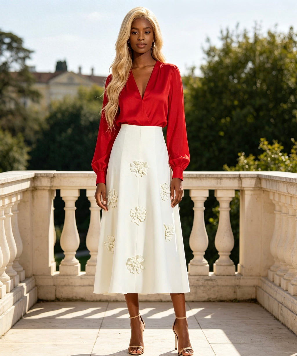 Woman wearing a red blouse and white skirt with floral embroidery on a balcony.