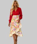 Woman wearing a red blouse and yellow floral skirt standing on a white background